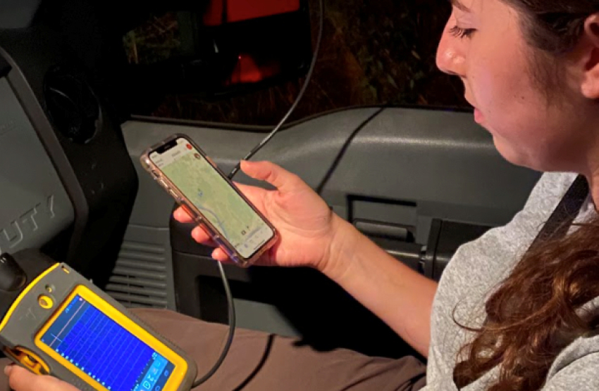 A woman sits in a car holding two mobile devices