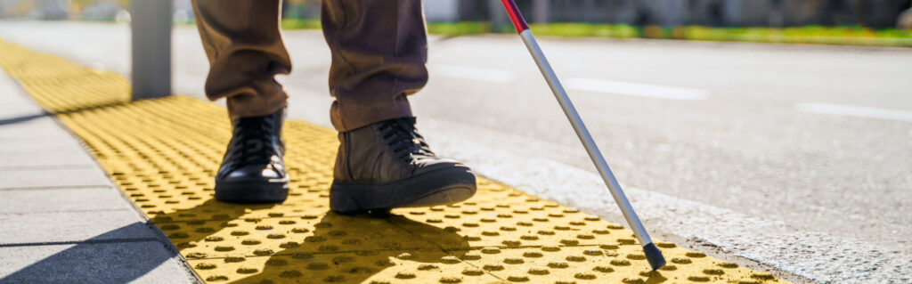 person with vision disability using a white cane to navigate the sidewalk